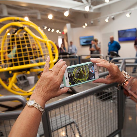 Visitors at Spaceport America observe a yellow spacecraft simulator in the facility's exhibition area.
