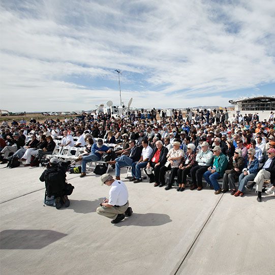 A large crowd gathers at Spaceport America for an event, with various support vehicles visible in the background.