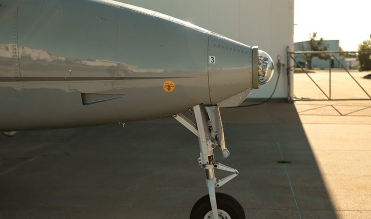 Close-up of the nose section and front landing gear of a grey aircraft parked on the tarmac at Spaceport America.